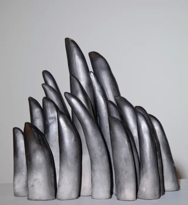 Cluster of silvery metallic sculptural forms resembling abstracted fingers or organic shapes, arranged on white surface.