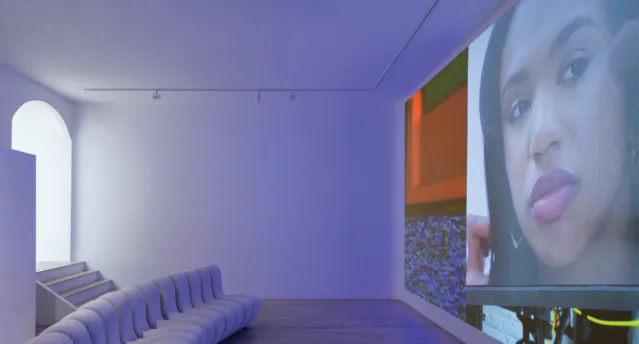 Gallery interior with purple ambient lighting, curved seating, video projection, and geometric architectural elements.
