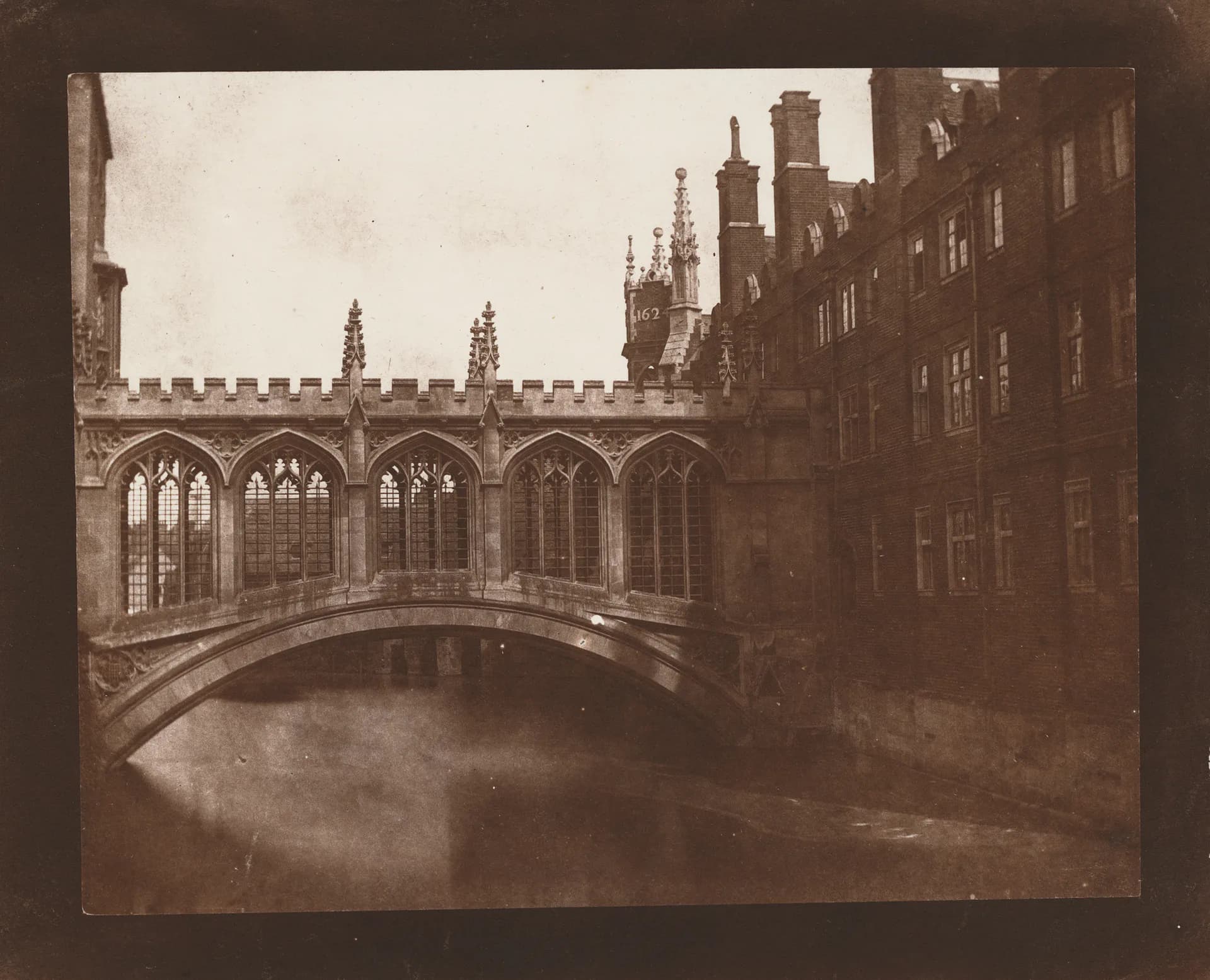 Sepia-toned photograph of Gothic bridge spanning a river between ornate stone buildings and spires.