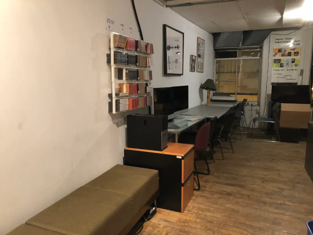 Harvestworks studio interior with workstations, shelving, wooden floor, and equipment visible in a bright white-walled space.