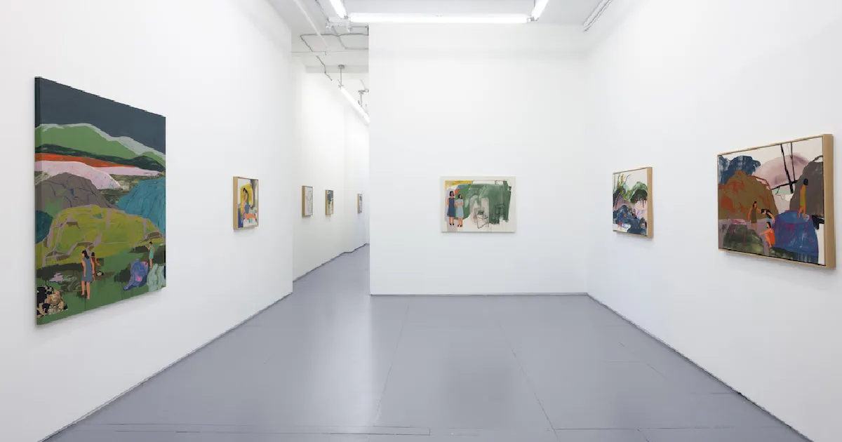 Gallery interior with white walls, gray floor, and several framed paintings displayed in a long hallway space