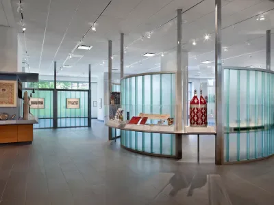 Gallery interior with glass partition displays, polished concrete floors, track lighting, and artwork mounted on walls in the background.