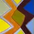 Abstract geometric painting with interlocking yellow, orange, blue, and red diagonal shapes forming a dynamic X-pattern composition.