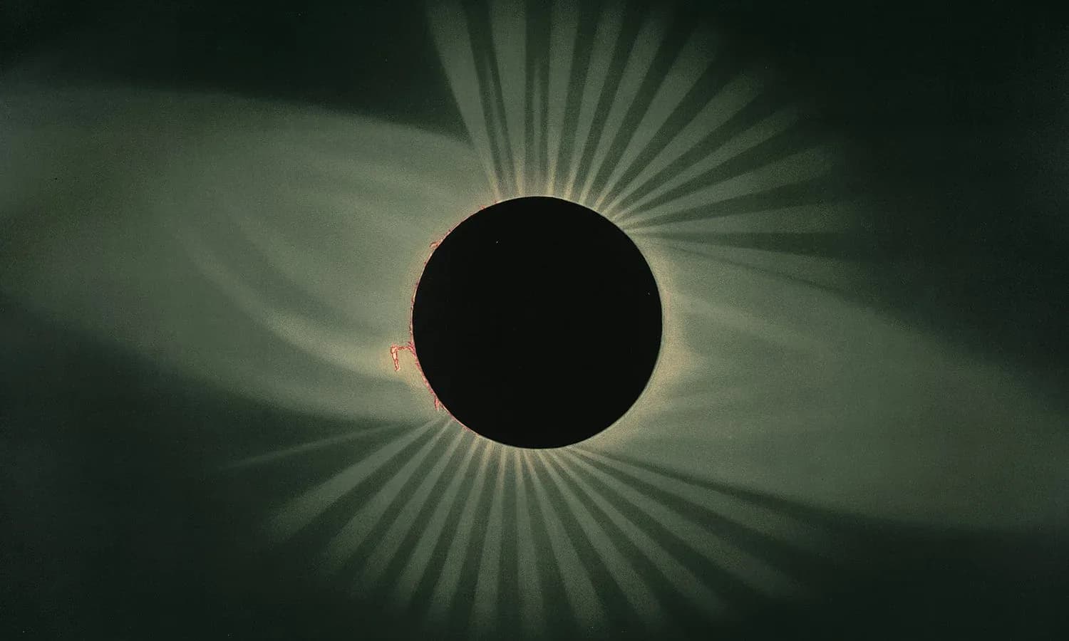 Total solar eclipse with black moon disk surrounded by radiating corona and solar rays against darkened sky.