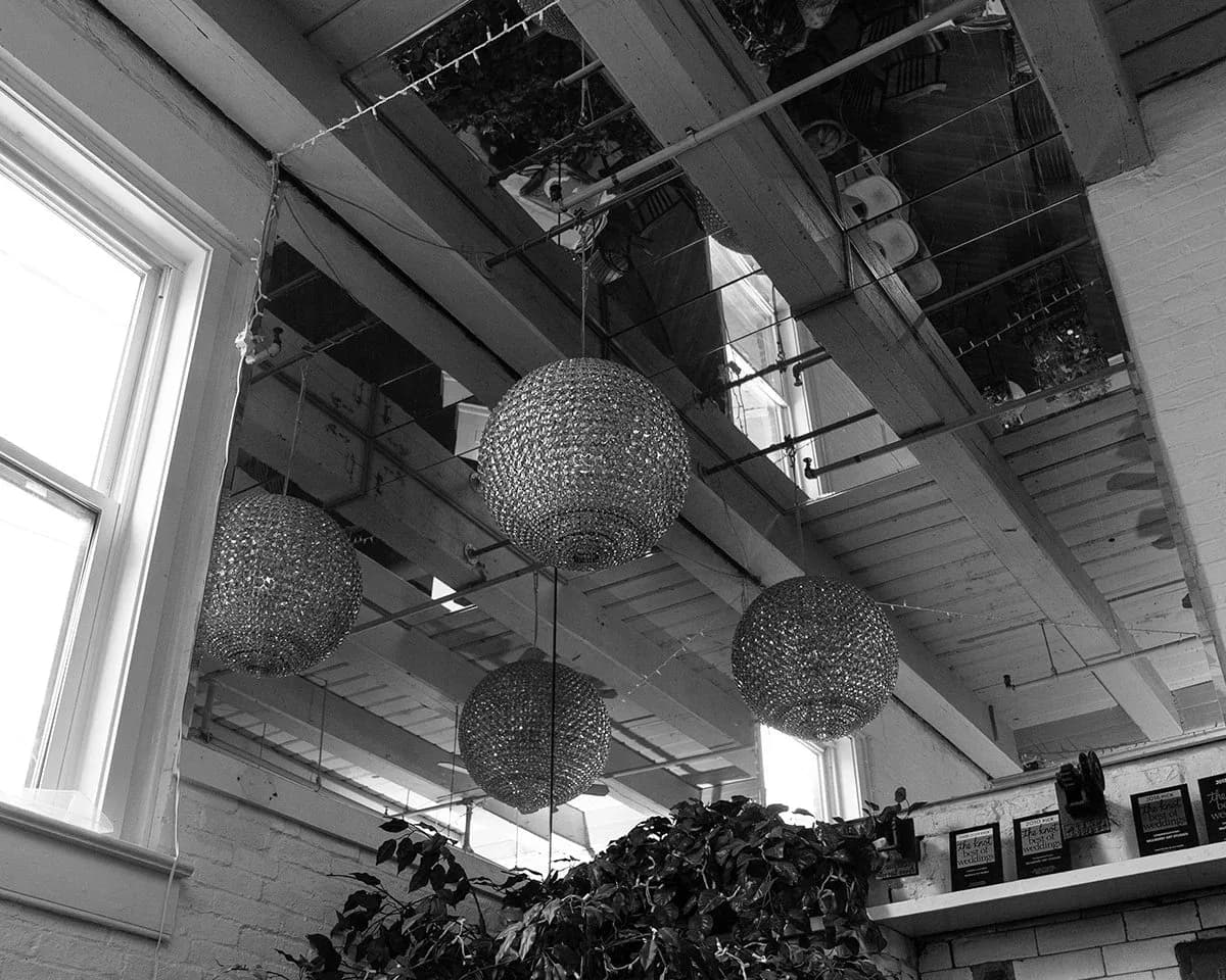 Interior of gallery space with geometric woven pendant lights hanging from ceiling, industrial beams, and natural light from windows.