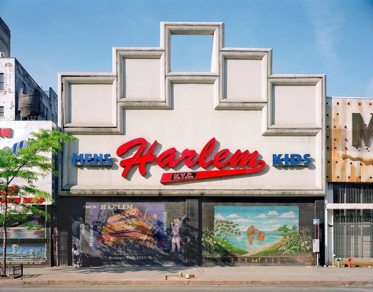 Storefront exterior of Harlem vintage clothing store with white facade, geometric window frames, red signage, and metal gates.