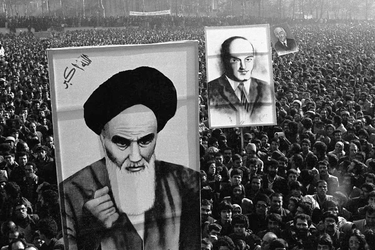 Black-and-white photo of a large crowd holding up portrait posters of a bearded cleric and another man during a political demonstration.