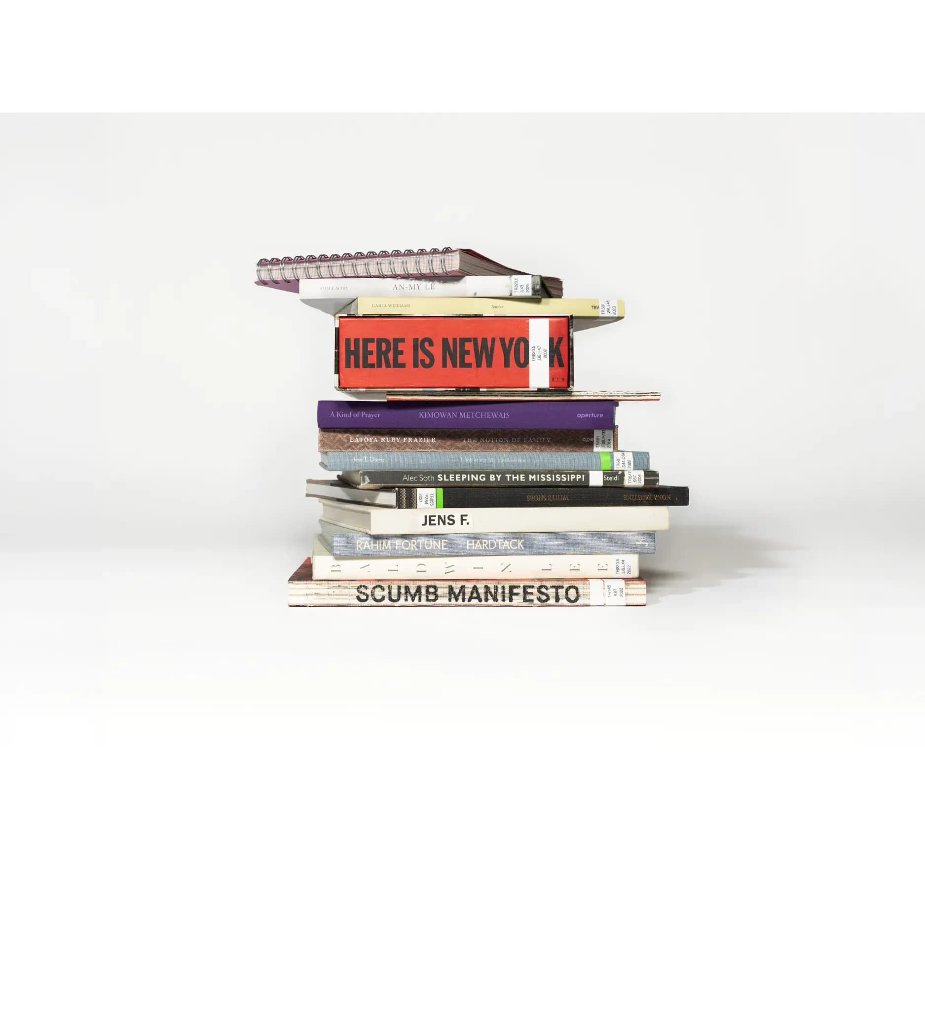 Stack of books and publications arranged vertically, including titles 'HERE IS NEW YORK,' 'SCUMB MANIFESTO,' and others, against neutral background.