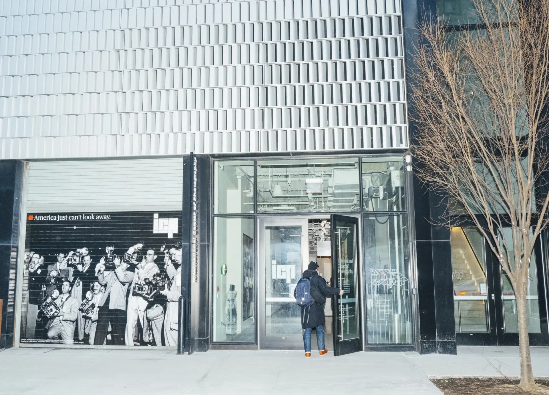 Storefront exterior of International Center of Photography with white corrugated metal facade, glass entrance doors, and person entering gallery space.