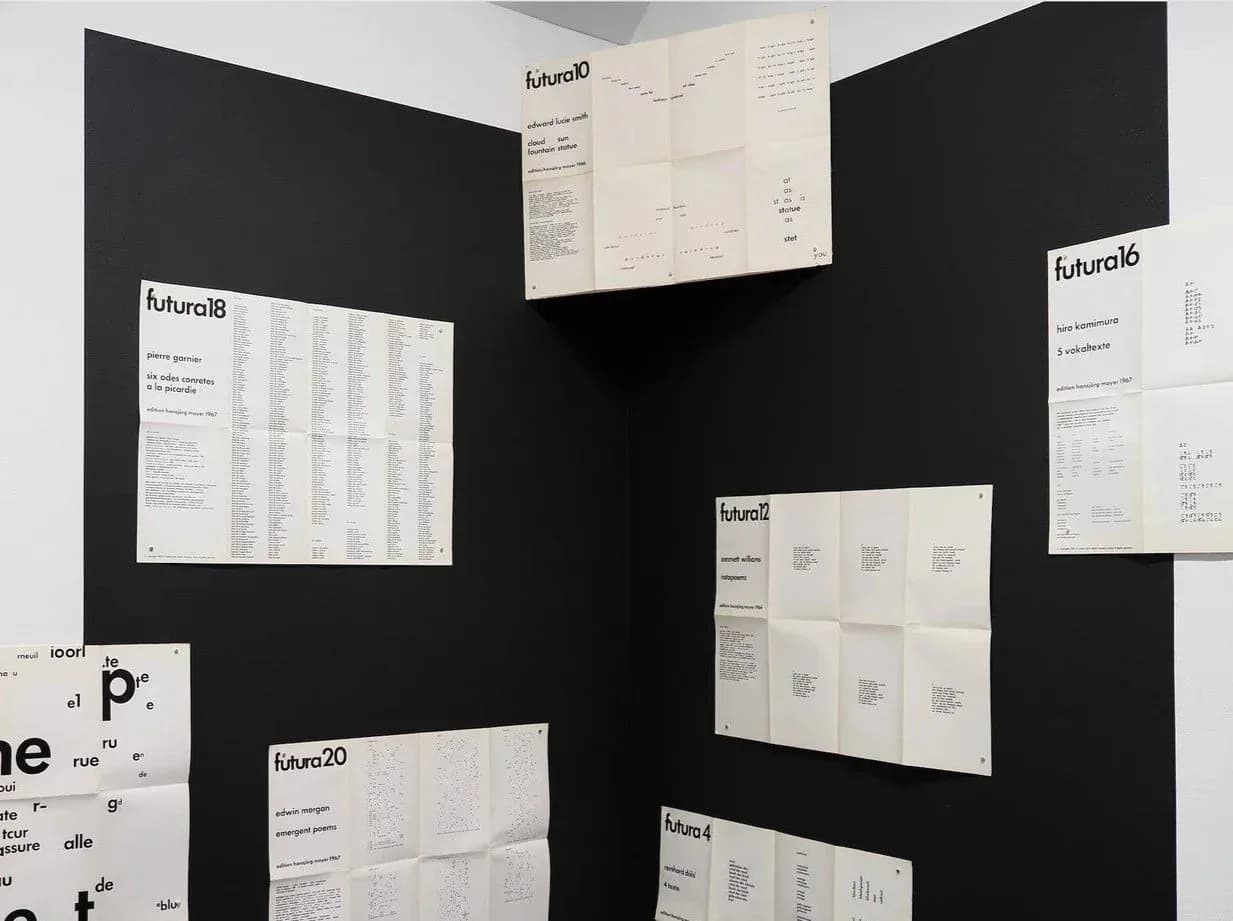 Gallery wall installation with black background displaying multiple framed white printed works and typography samples, labeled "futuro18" and other series.