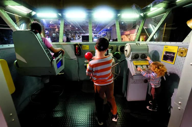 Interactive museum flight simulator cockpit with children at control stations under bright overhead lighting.