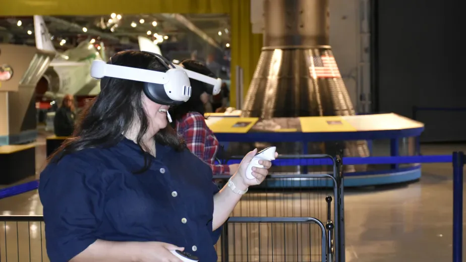 Visitor wearing VR headset experiencing interactive exhibit at Intrepid Museum Foundation with aircraft engine visible in background.