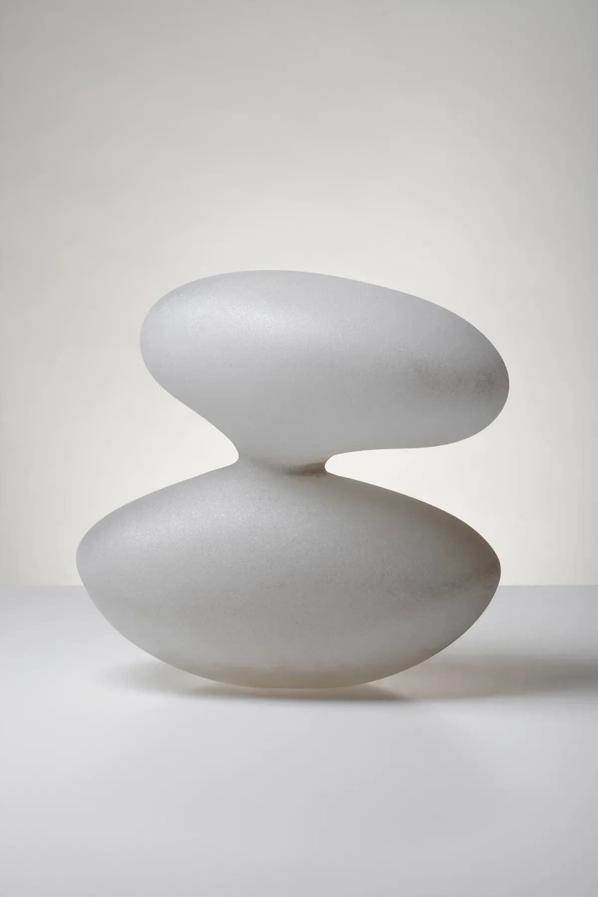 Abstract white ceramic or plaster sculpture with two stacked elliptical forms creating a balanced, minimalist composition against neutral background.