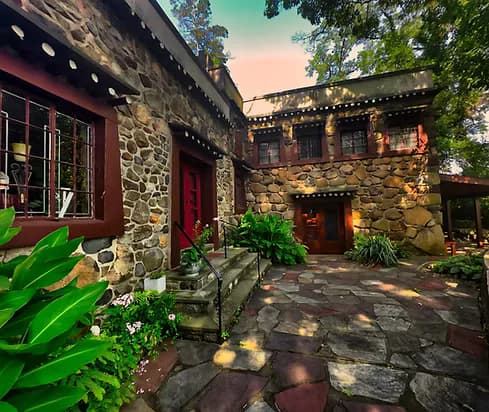 Stone and red-painted courtyard of Jacques Marchais Center with arched doorways, tropical plants, and evening lighting.