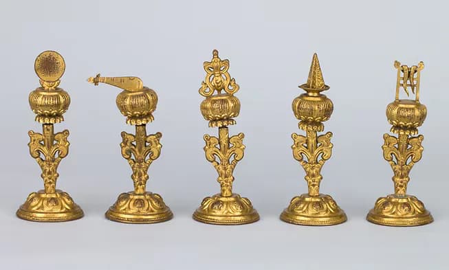 Five ornamental brass Buddhist ritual finials with tiered spheres and decorative bases on golden pedestals.