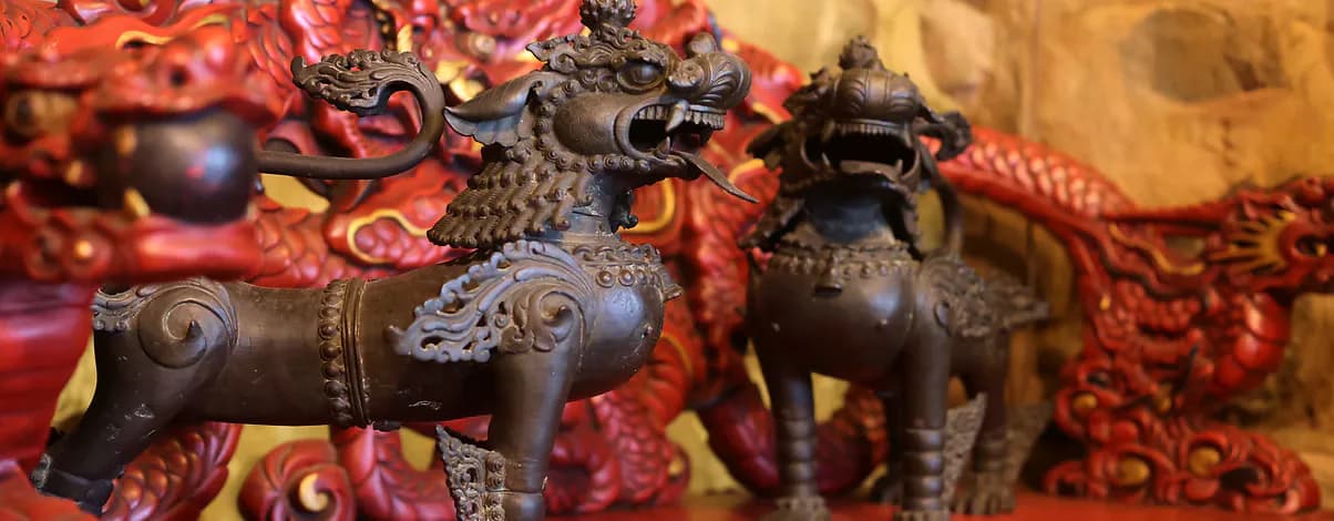Dark bronze animal figurines with red and ornate textile backdrop, depicting Tibetan decorative objects.