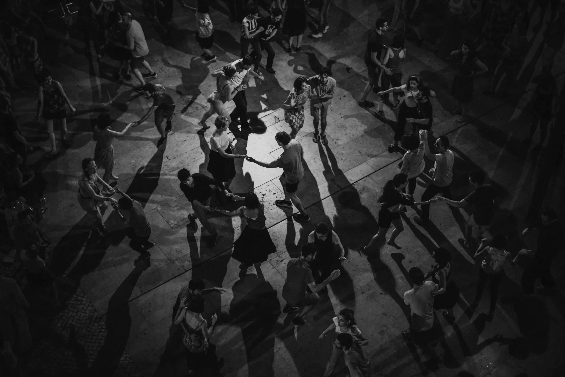 Black and white overhead photograph of figures arranged in circular formation on ground with dramatic shadows and lighting.