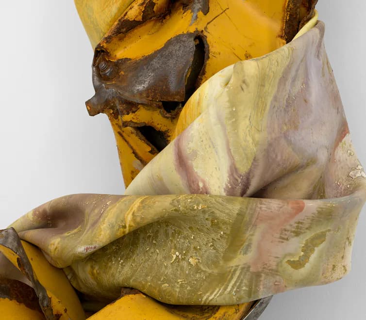 Wrapped textile or fabric sculpture in cream and pale colors draped around a yellow and dark brown wooden abstract form, creating organic, folded shapes.