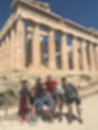Blurred exterior photograph of a classical building with columns and people standing in front, possibly a museum or institutional building.
