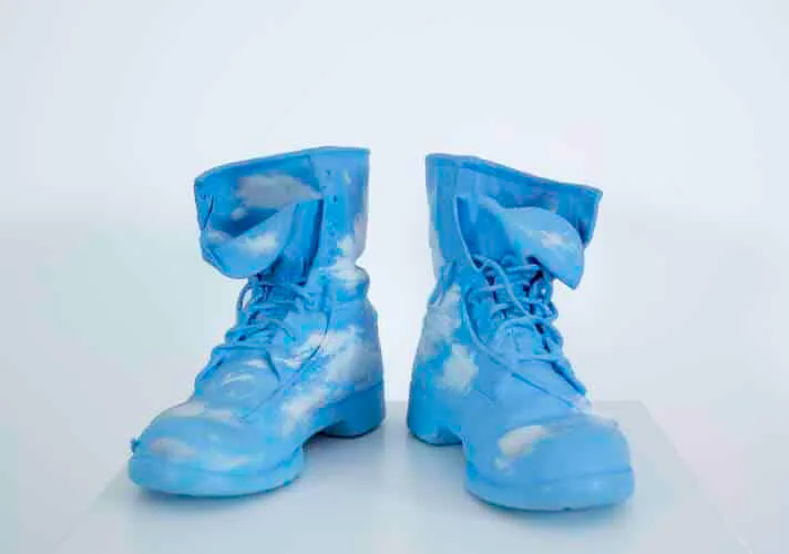 Pair of bright blue sculptural boots with cloud-like white patterns, displayed on white surface against white background.