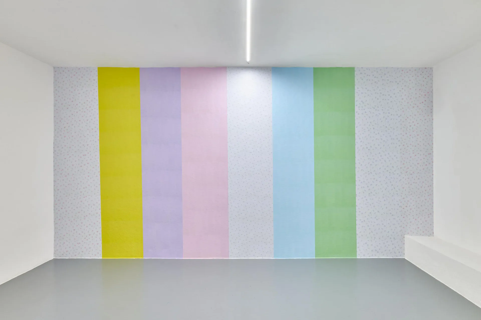 Installation of six vertical colored panels on white wall: yellow, lavender, pink, white, light blue, and green stripes with subtle light reflection.