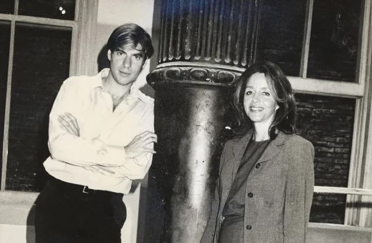 Black and white photograph of two people standing beside a large cylindrical sculptural element in an interior space.