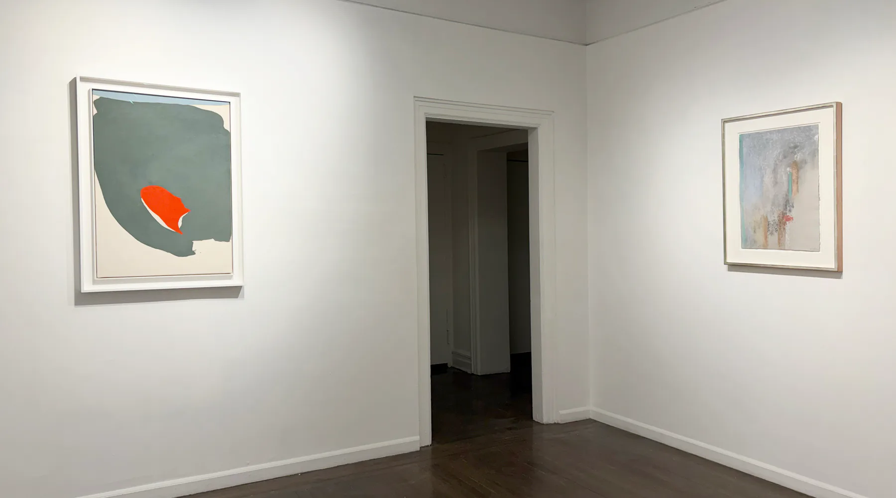 Gallery corner with white walls, dark floor, doorway, and three framed artworks: left frame contains gray-blue abstract work with orange element.