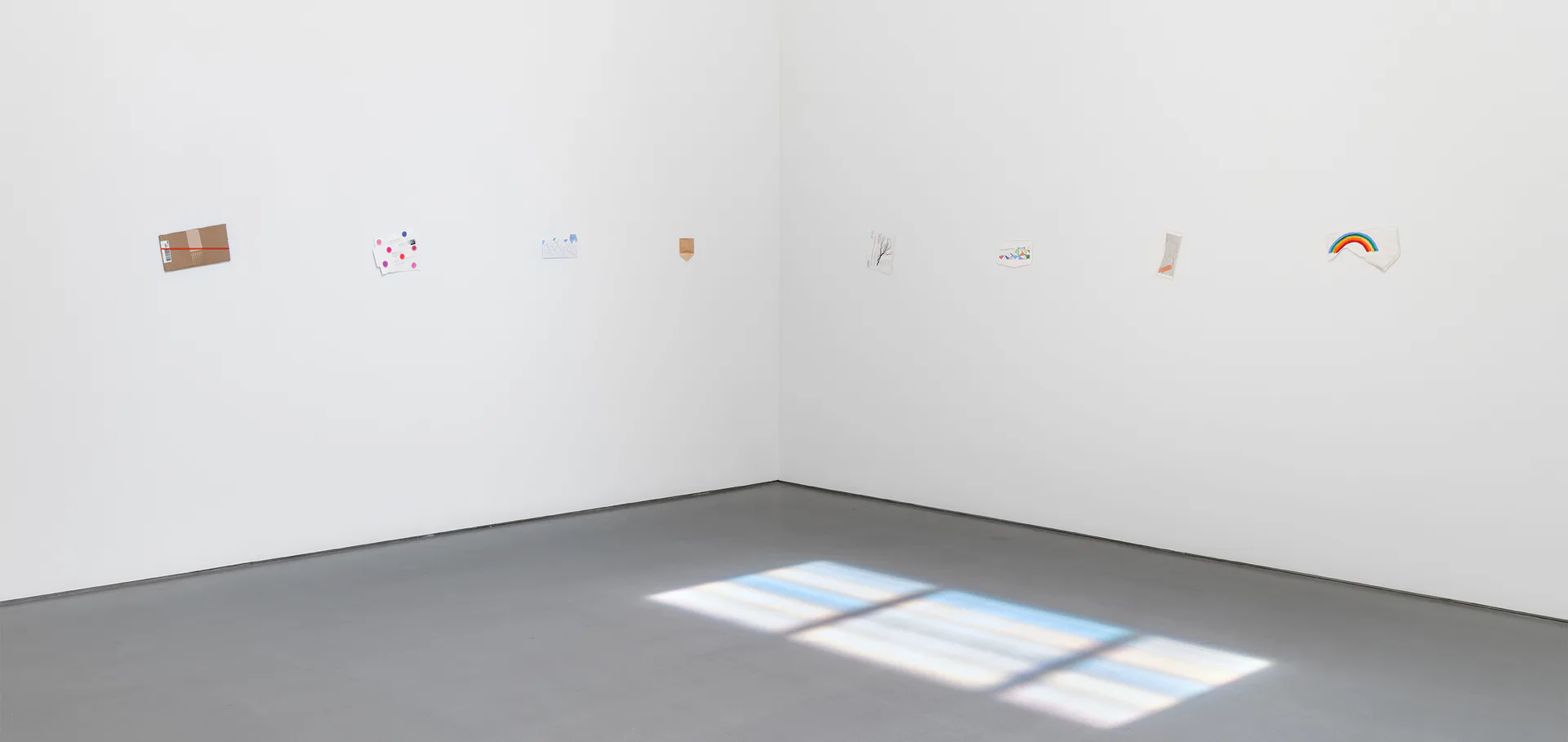 Lisson Gallery interior with gray polished floor, white walls, and small artworks displayed on upper wall ledge; bright window light casts rectangular patterns on floor.