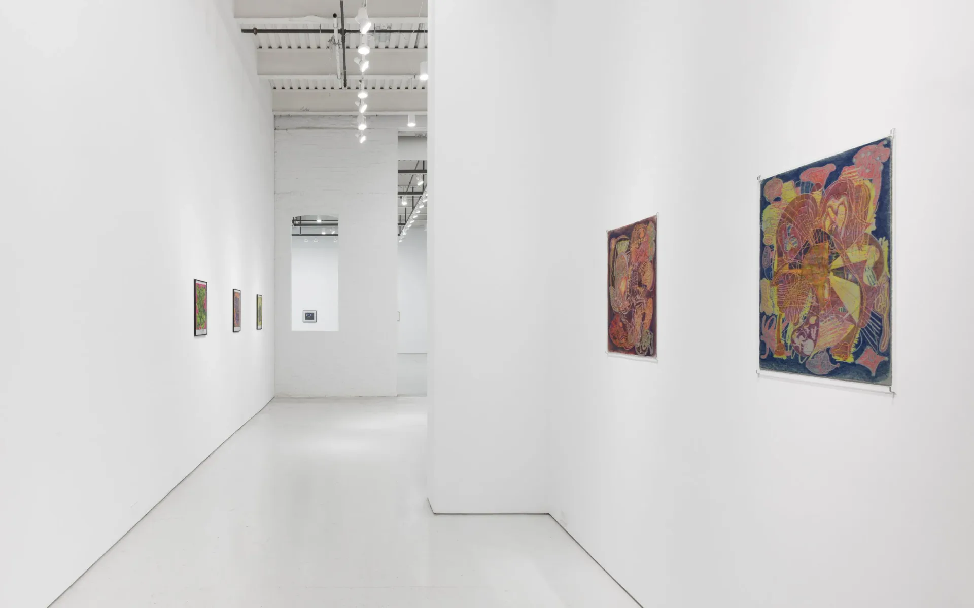 White gallery corridor with minimal framed artworks on walls and industrial ceiling elements visible.
