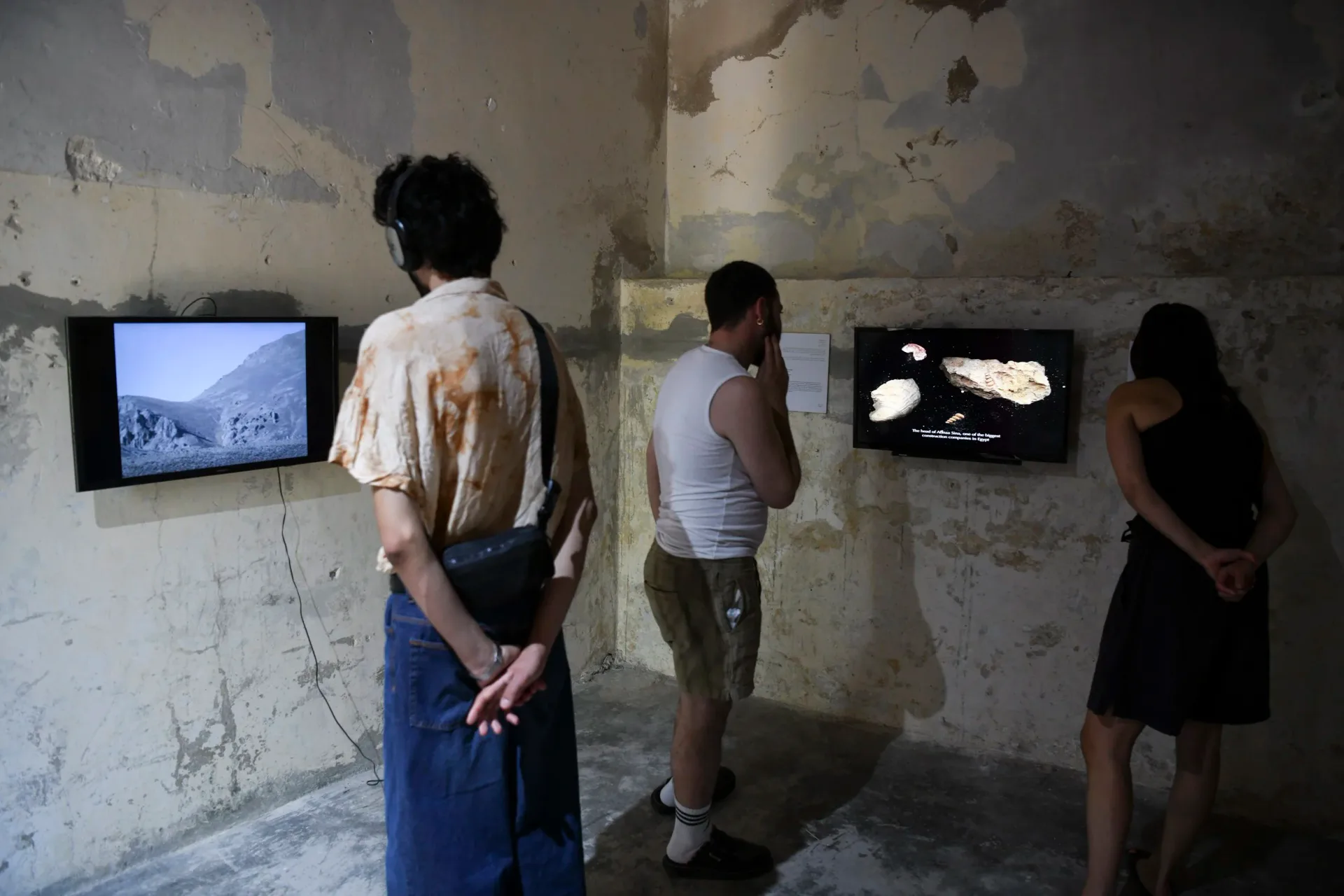 Interior gallery space with weathered walls displaying small framed monitors; visitors viewing work at Magnum Cultural Foundation.