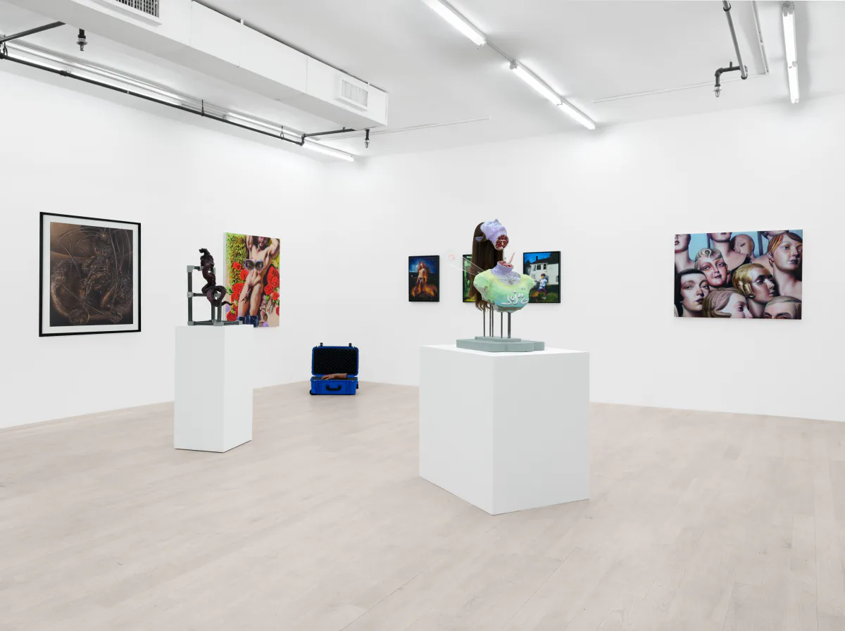 Minimalist gallery space with white pedestals displaying sculptures and mixed-media works, framed photographs and paintings on white walls.