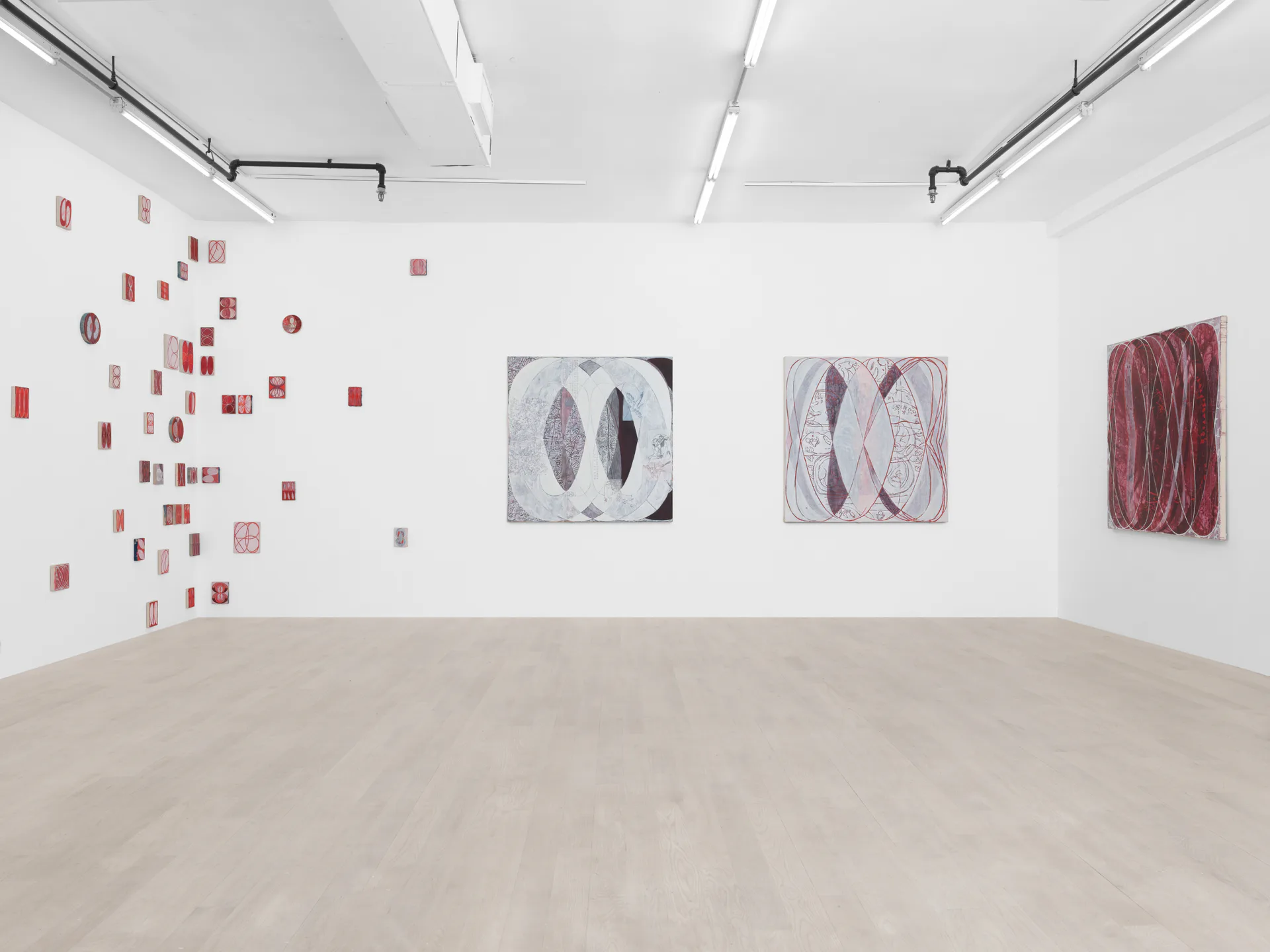 Management gallery with abstract textile and photographic works: scattered pink geometric forms on left wall, three larger framed pieces on right wall.