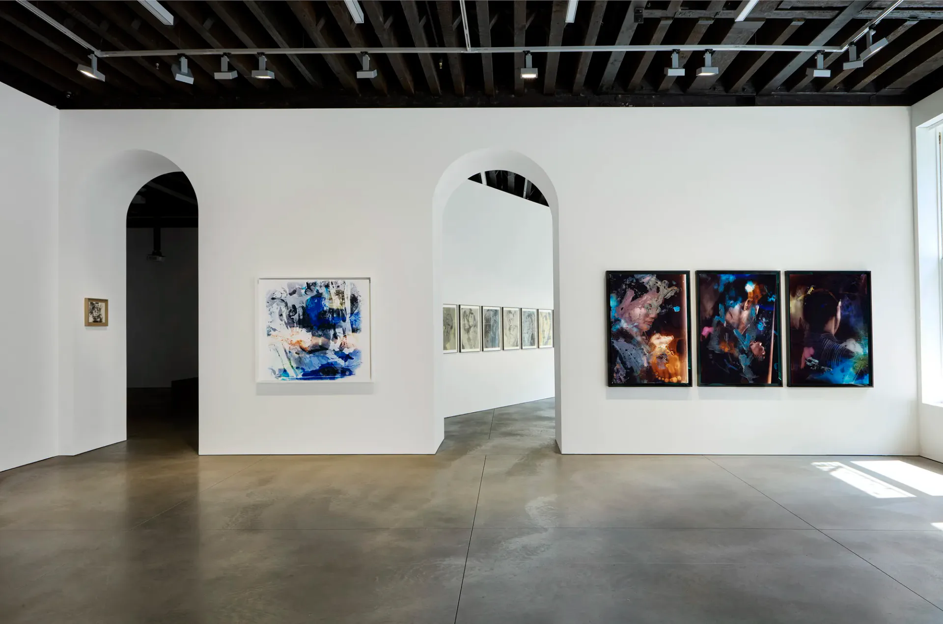 Interior of Marian Goodman Gallery showing white walls, polished concrete floor, arched doorway, and various artworks on display.