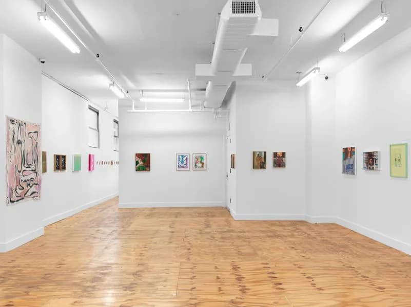 Marinaro gallery interior with exposed ceiling fixtures, blonde wood floors, white walls displaying diverse small and medium artworks including abstract and figurative pieces.