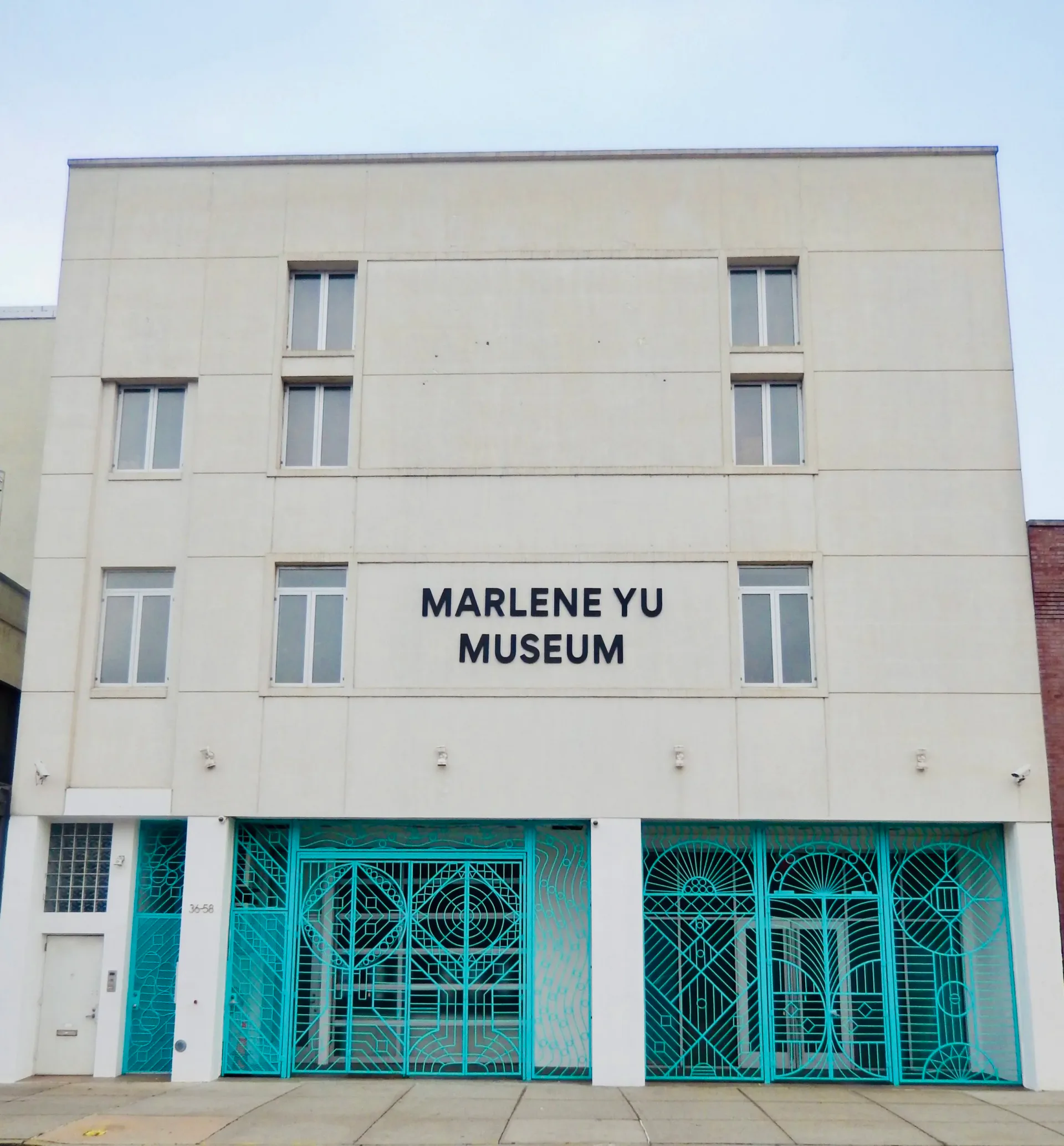Exterior facade of Marlene Yu Museum with beige walls, upper windows, and ornate teal decorative gates at the storefront entrance