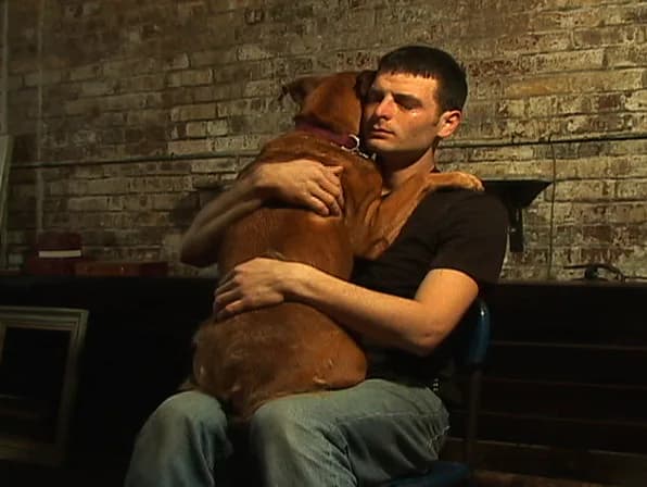 Man in brown shirt holding brown dog against brick wall interior, photograph-as-art.