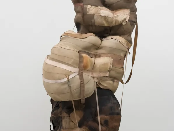 Torso wrapped in tan and white gauze bandages against dark lower body, sculptural mixed-media work.