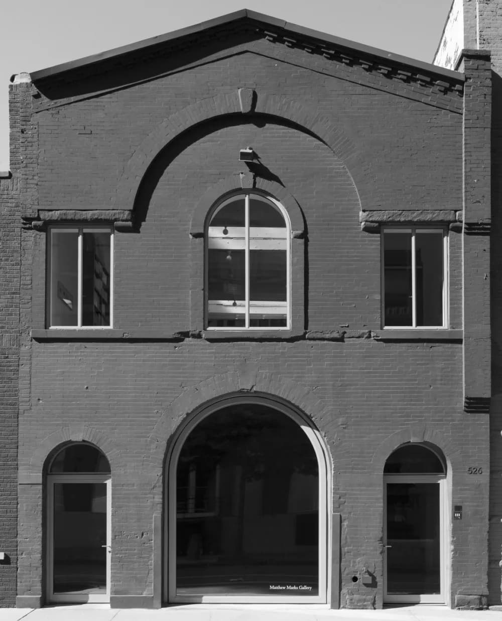 Brick facade of Matthew Marks Gallery with large arched windows and glass entrance doors