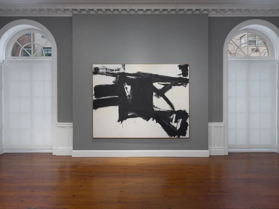 Gallery interior with gray walls, arched doorways, and abstract black and white artwork mounted centrally on wall.