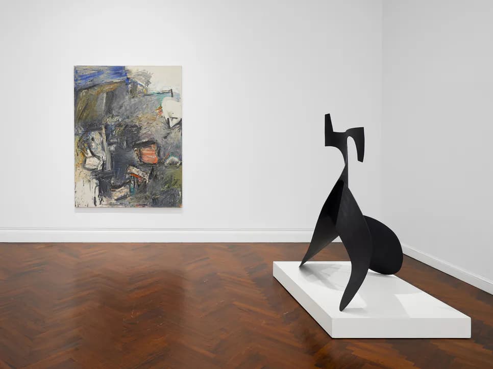 Gallery interior with mixed-media painting on left wall and black abstract sculpture on white pedestal at right.
