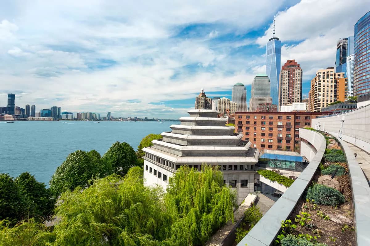 Modern cruise ship docked at Manhattan's West Side with New York City skyline and Hudson River visible in background.