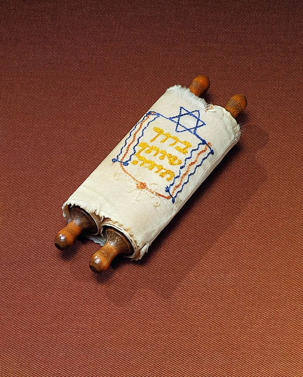 Torah scroll textile artwork with white linen fabric, embroidered Star of David and Hebrew text in blue and gold, wooden rollers at ends.