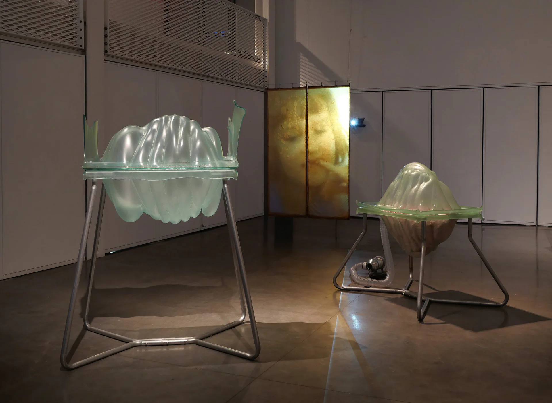 Two translucent sculptural forms on metal stands with internal illumination in gallery space; mixed-media installation with organic, flowing shapes.