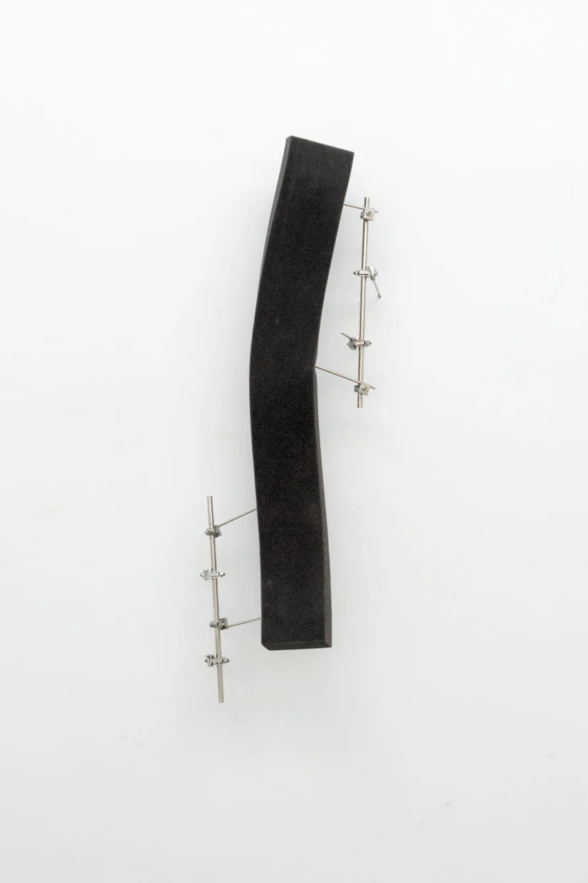 Curved black textile or material piece mounted on white wall with silver metal rod attachments; minimalist sculptural work.