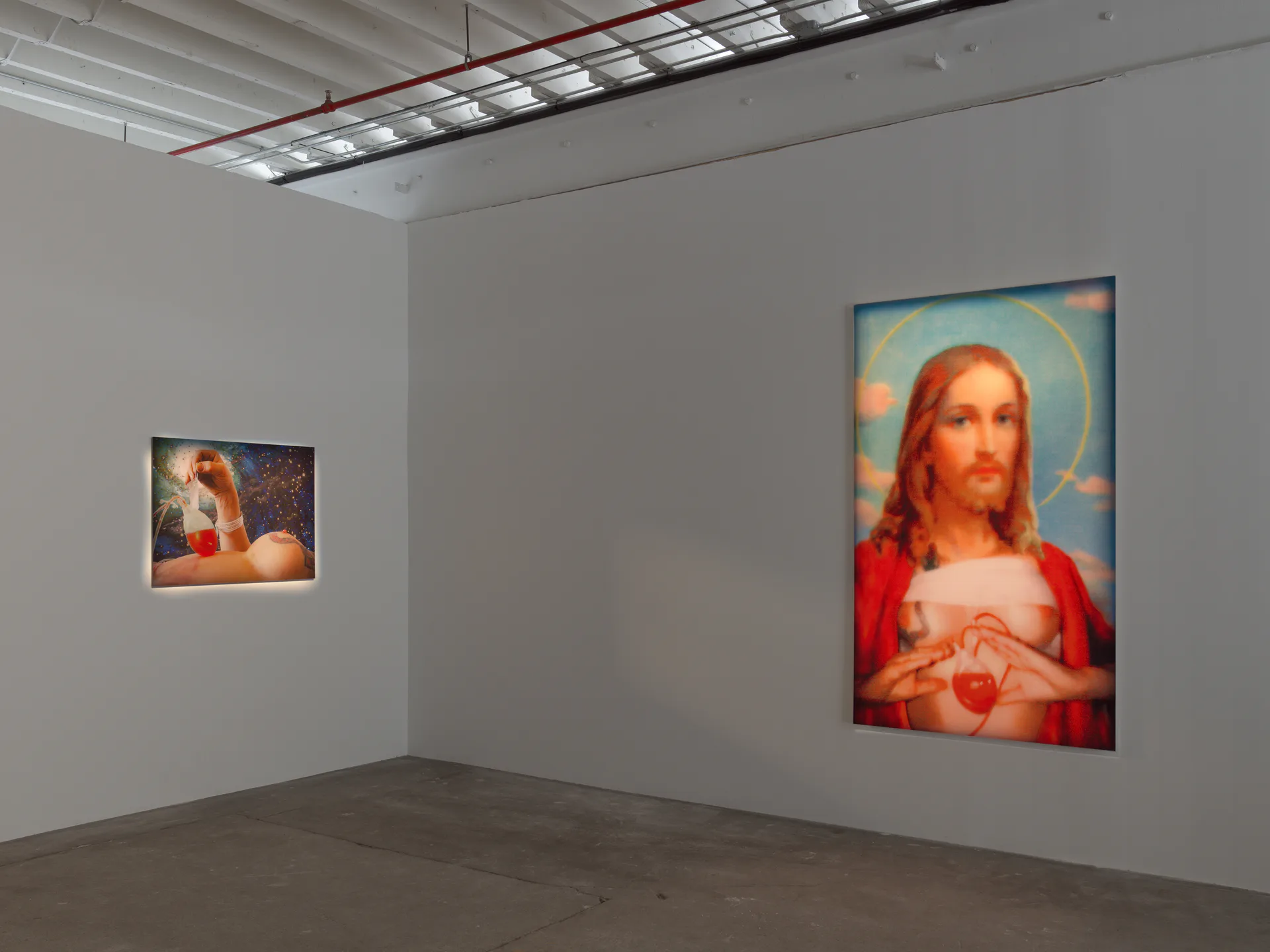 Gallery interior with white walls displaying two religious-themed artworks featuring figures with halos and red robes.