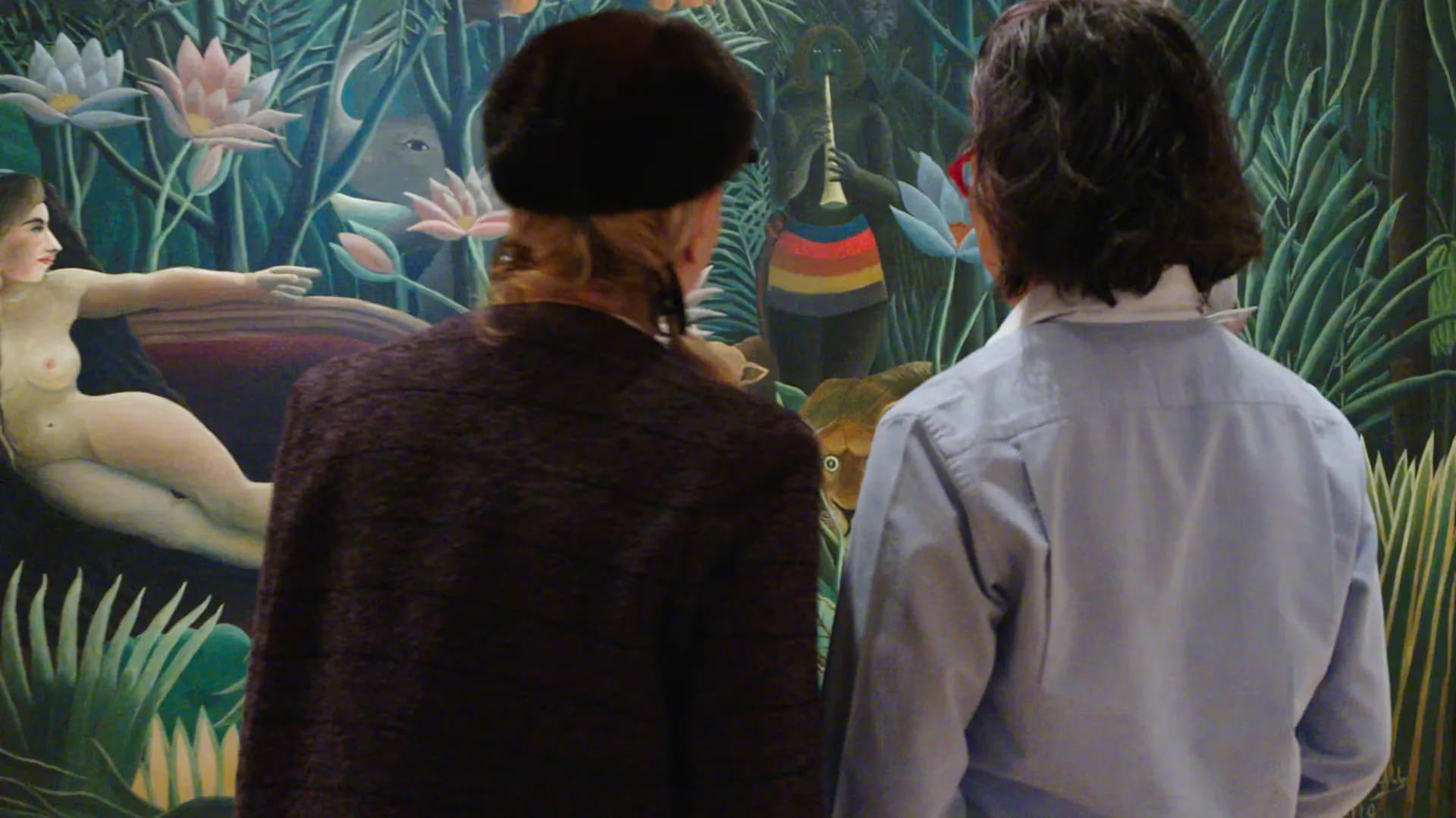 Two visitors from behind viewing a vibrant mural with jungle foliage, water lilies, and hanging sculptural elements in gallery space.