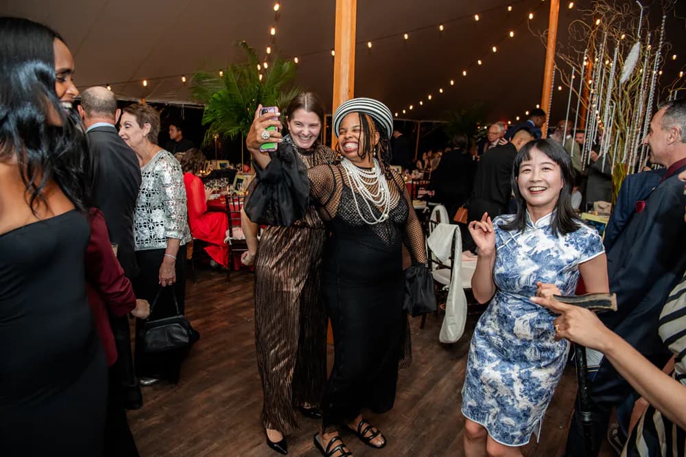 Indoor evening event with attendees mingling under warm string lights and industrial ceiling structure.