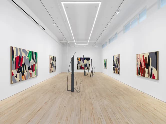 Modern gallery corridor with light wood flooring, neon geometric ceiling installation, and abstract paintings in bold geometric compositions lining walls.