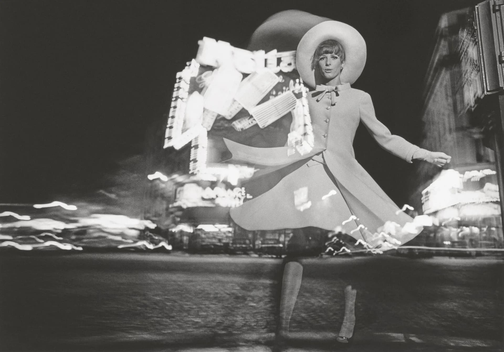 Black-and-white photograph of a woman in a white dress and sun hat sitting by water, appearing to be a still from a classic film.