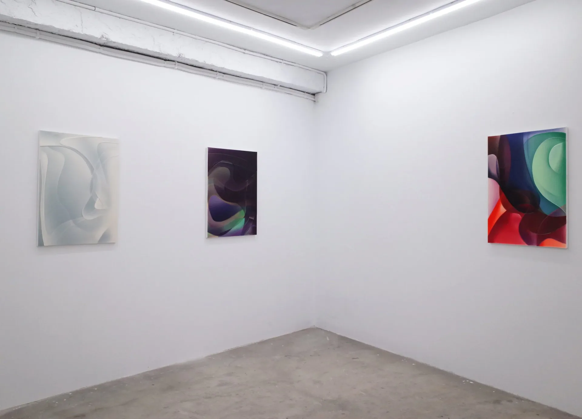White gallery wall with three abstract paintings in varying color palettes—pale, dark purple, and vibrant red-blue-green—displayed at intervals.